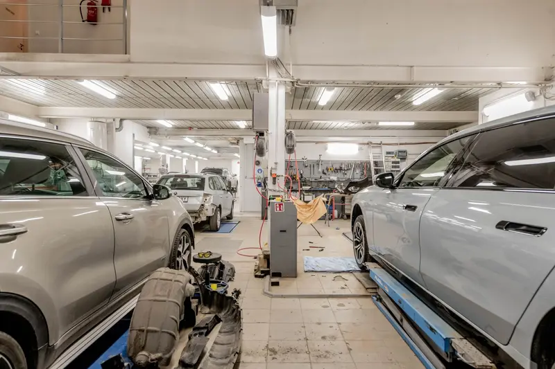 Interior de oficina mecânica com dois carros em serviço e o box ao fundo